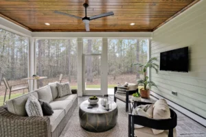 Modern screened porch with wood ceiling, glass walls, and cozy neutral seating overlooking nature.