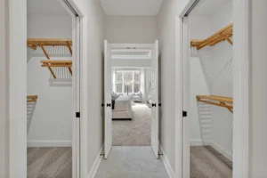 Bright modern walk-in closet hallway with wooden shelving leading to a sunlit minimalist bedroom.
