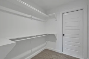 Minimalist white walk-in closet with shelves, hanging rods, and beige carpet flooring.