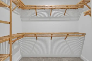 Bright modern walk-in closet with white walls, light wood shelving, and gray carpet flooring.