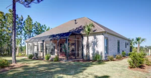 Modern brick house with screened porch, green lawn, and tall pine trees under blue sky.