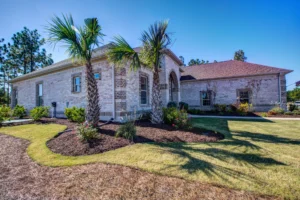 Single-story stone home with palm trees and landscaped yard under a clear blue sky.