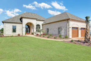 Modern single-story stone and brick home with arched entryway and wooden garage under blue sky.