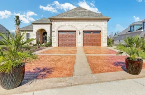Modern stone suburban home with dual wooden garages and palm planters under a sunny sky.
