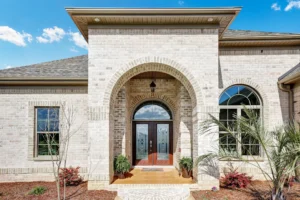 Modern light brick home with arched doorway, wooden double doors, and elegant front landscaping.