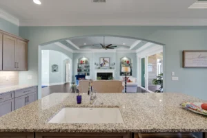 Modern open-concept kitchen and living room with granite island, soft tones, and central fireplace.