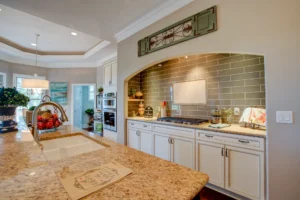 Bright modern kitchen with granite island, white cabinets, and stylish gray backsplash.