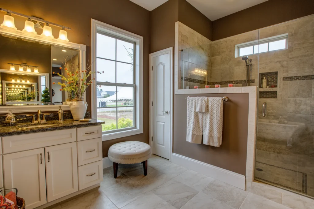 Modern master bathroom with granite vanity, glass shower, and warm natural lighting.