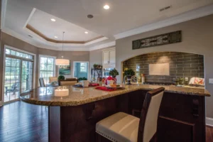 Modern open kitchen with granite island, wood floors, and bright dining area with large windows.