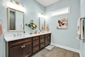 Modern blue bathroom with double vanity, dark wood cabinets, and warm orange floral accents.