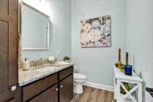 Modern coastal bathroom with soft blue walls, wood flooring, and elegant gold and floral accents.