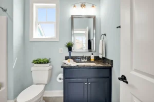 Small modern bathroom with light blue walls, navy vanity, granite countertop, and natural lighting.