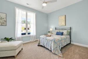 Cozy coastal bedroom with light blue walls, patterned bedding, and soft natural sunlight.