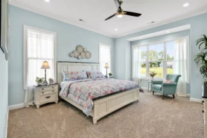 Light blue cottage bedroom with white bed, floral bedding, and bright bay window reading nook.