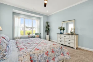 Pastel blue bedroom with floral bedding, white furniture, and bright bay window seating.