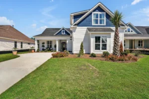 Modern blue and white coastal home with palm tree, large windows, and sunny landscaped exterior.