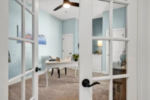 Modern light blue coastal home office with French doors, white desk, and nautical décor.