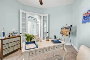 Coastal home office with light blue walls, vintage white desk, and natural light through French doors.
