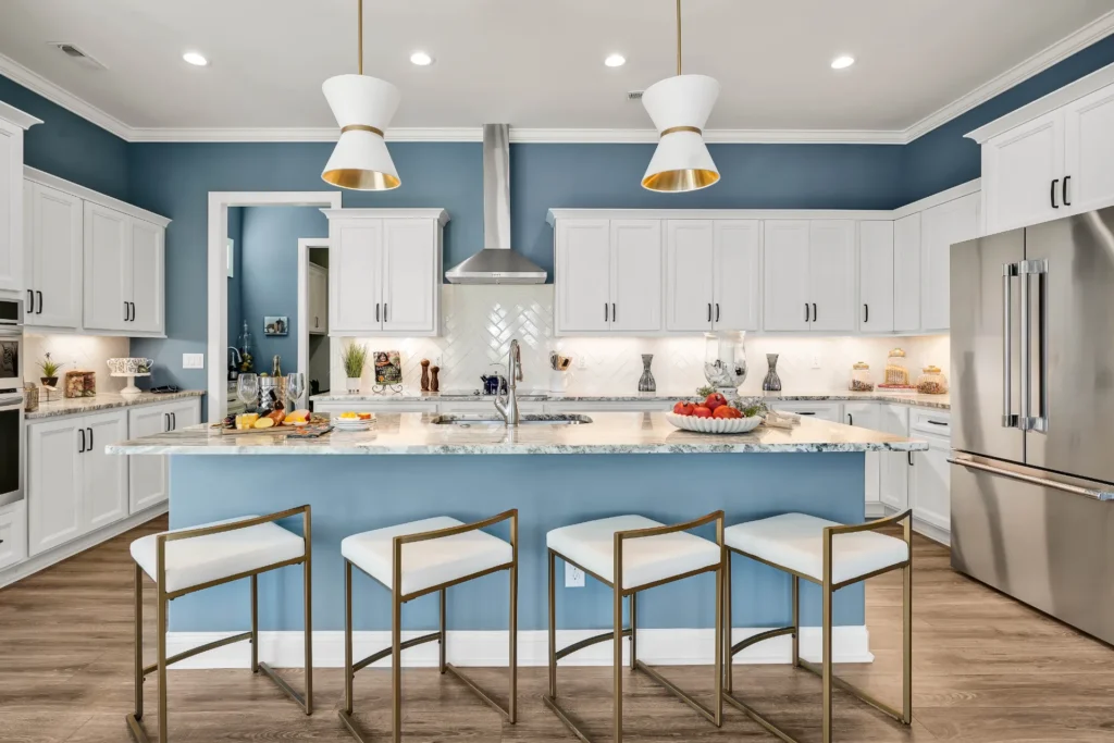 Modern blue and white kitchen with marble island, gold accents, and stainless steel appliances.