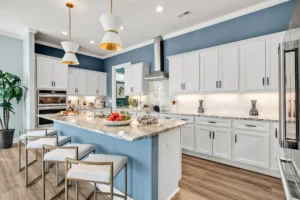 Modern white kitchen with blue island, gold accents, granite countertops, and stainless steel appliances.