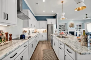 Bright modern kitchen with white cabinets, marble island, pendant lights, and warm wood flooring.