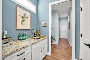 Modern blue kitchenette with white cabinets, granite countertop, and warm wood floors.