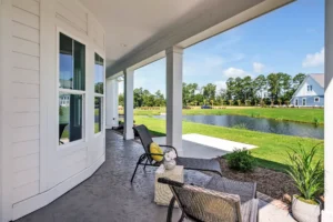Modern covered patio with wicker chairs overlooking a tranquil pond and lush green landscape.