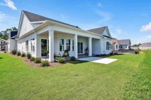 Modern white farmhouse with covered porch, dark roof, and lush lawn in sunny suburban neighborhood.