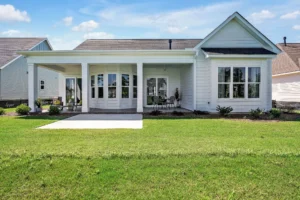Modern white farmhouse with gable roof, columned porch, dark accents, and green lawn under blue sky.