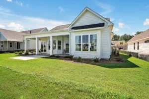 Modern white farmhouse with gable roof, large windows, and covered patio in suburban setting
