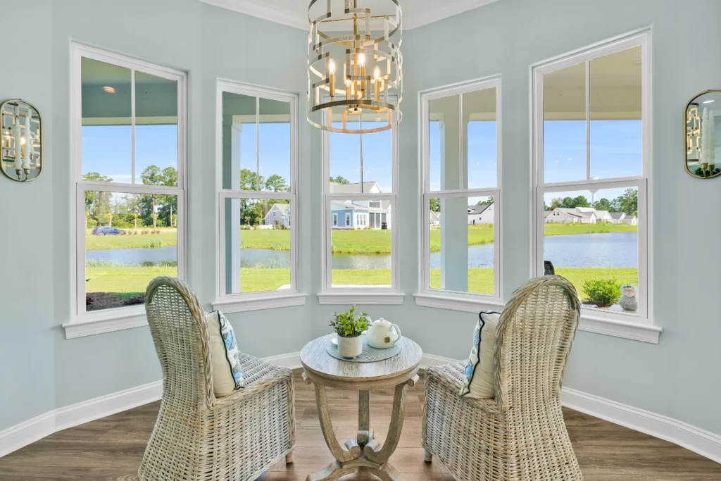 Bright coastal sunroom with wicker chairs, blue walls, and panoramic lake view.