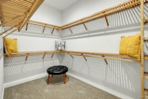 Modern bright walk-in closet with light wood shelving, beige carpet, and stylish decorative accents.