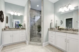 Modern bathroom with glass shower, dual white vanities, granite countertops, and elegant symmetrical design.