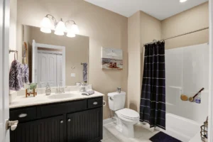 Modern beige bathroom with black vanity, white tub-shower combo, and stylish dark checkered curtain.