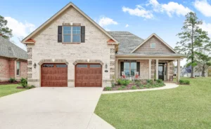 Elegant brick and stone ranch home with porch, wooden garage doors, and lush green lawn.