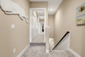 Modern beige hallway with gray carpet, white trim, and staircase in contemporary home interior.