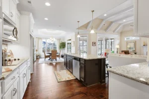 Modern open-concept kitchen with white cabinets, dark island, hardwood floors, and natural light.