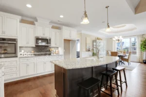 Bright modern kitchen with white cabinets, quartz island, stainless steel appliances, and warm wood flooring.