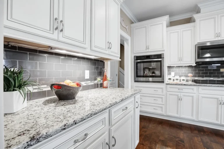 Bright modern white kitchen with granite countertops, dark backsplash, and sleek built-in appliances.