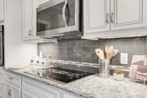 Modern white kitchen with gray subway tile backsplash, granite countertops, and stainless steel appliances.