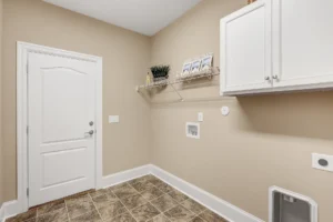 Modern beige laundry room with white cabinets, tile flooring, and washer dryer hookups.