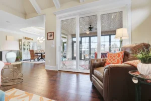 Bright open-concept living room with leather armchair, hardwood floors, and sunlit adjoining sunroom.