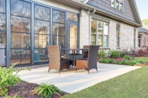 Modern brick patio with wicker furniture, large windows, and lush landscaped greenery.