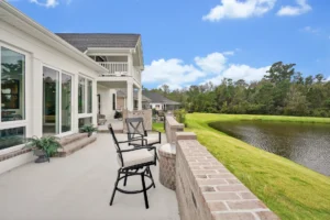Modern lakeside patio with cushioned seating overlooking tranquil pond and contemporary white home exterior.
