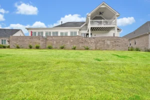 Modern two-story suburban home with covered balcony, stone wall, and green backyard lawn.