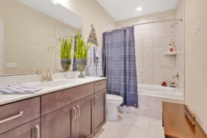 Modern beige bathroom with dark wood vanity, blue shower curtain, and green plant accents.