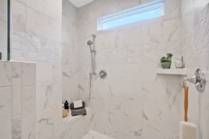 Modern walk-in shower with white marble tiles, chrome fixtures, and a small green plant.