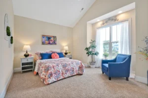 Bright airy bedroom with floral bedding, natural light, blue armchair, and cozy modern décor.