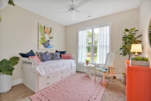 Bright cozy bedroom with coral dresser, tropical wall art, and colorful pillows.