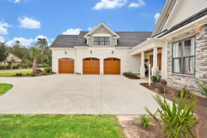 Elegant suburban house with three-car wooden garage, stone porch, and landscaped yard under blue sky.